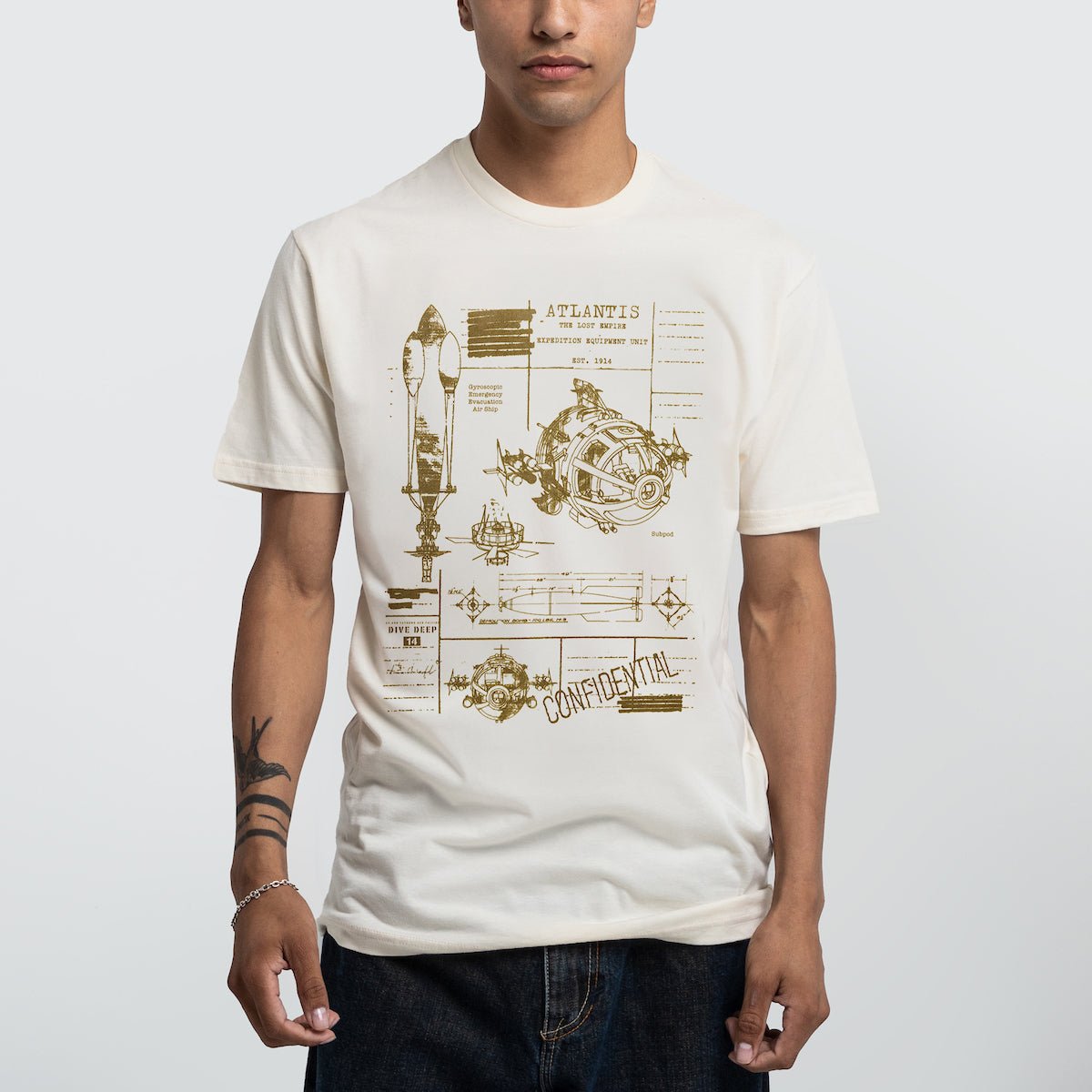 Man in a beige tee with Blueprint-style illustration of vehicles and diagrams for an Atlantis expedition.