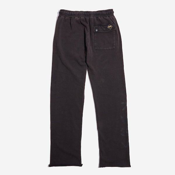 The back of dark grey sweatpants with an elastic waistband, featuring a back pocket with button closure and a vertical "rebel" graphic printed in distressed black text along the lower left leg.