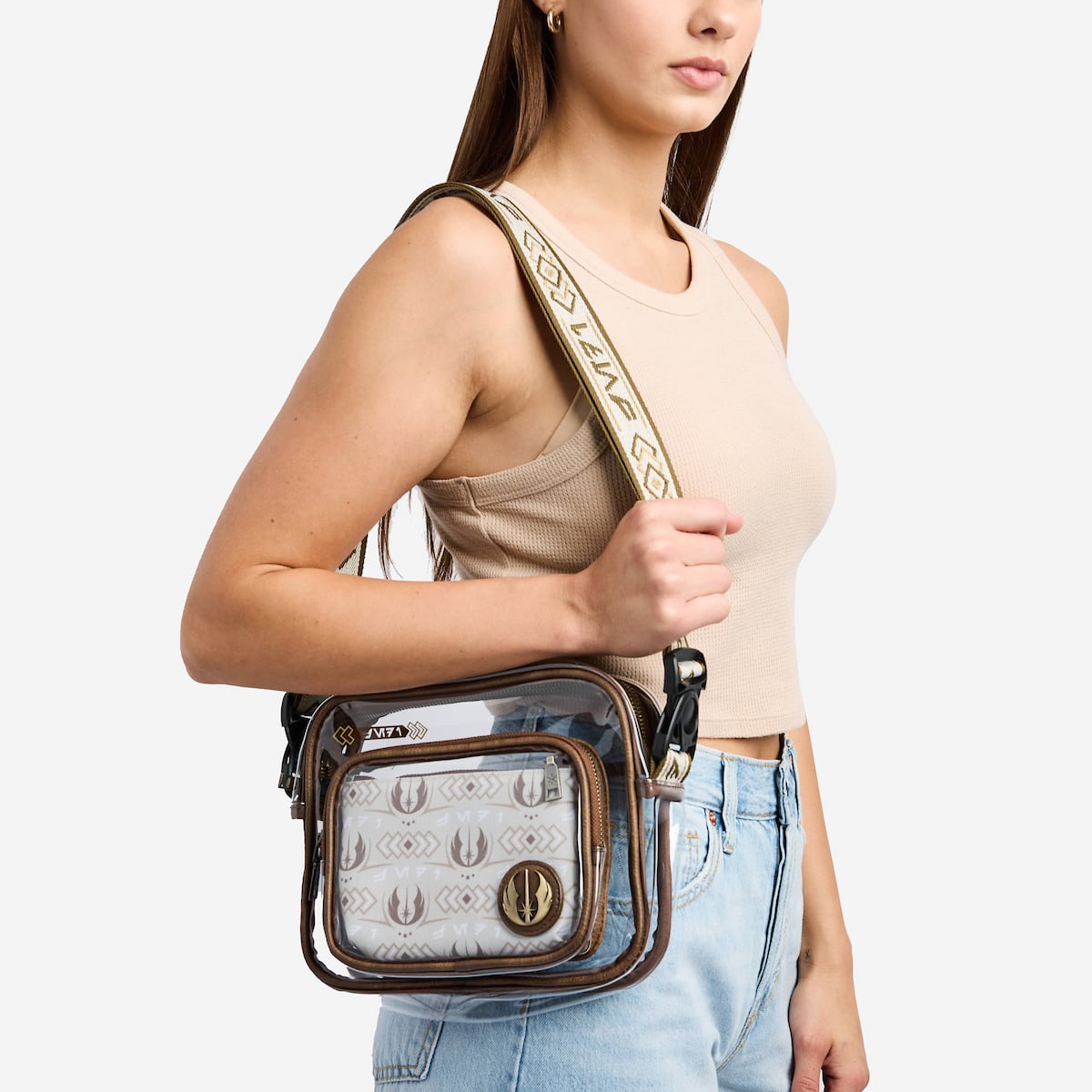 Woman holding a clear jedi crossbody bag with a patterned strap against a plain background