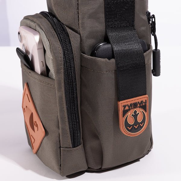 The photo shows a close up of a pocket on the bag. The pouch has a black strap with orange rubber on the end. The Orange Rubber has raised black art to showcase the Rebel logo.