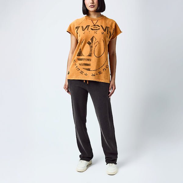 A woman dressed in an orange sleeveless crew neck and black wide leg sweatpants, featuring a Star Wars Rebel themed lounge set