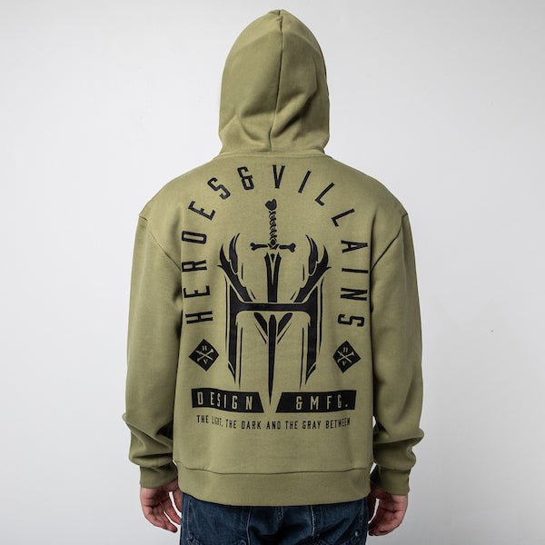 The picture shows a man standing backwards to show the back of a green hoodie. The print on the back is in a tombstone shape and features a large logo of an "H" and "V" with a dagger going through. The words "Heroes & Villians" arch over the design in an arch shape.