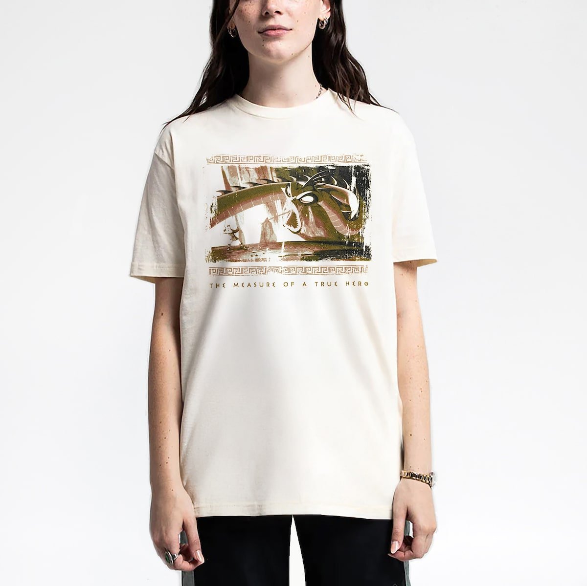 Woman in a beige tee with an Illustration of Hercules facing a Hydra with the text "THE MEASURE OF A TRUE HERO" below