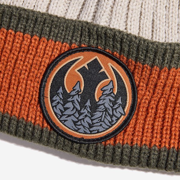 Photo shows a close up of the beanies cuff. There is a wide orange stripe between two smaller dark green stripes on the top and bottom. There is a patch embroided on the center of the cuff. The patch features the REBEL emblem from Star Wars with a wooded motif within the Rebel emblem.