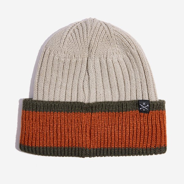 Photo shows a beige knit beanie. This beanie has a folded cuff that has a wide orange stripe between two smaller dark green stripes on the top and bottom. There is a small woven tag on the top of the cuff to the right that has the letters "H" and "V" to represent the brand Heroes and Villains