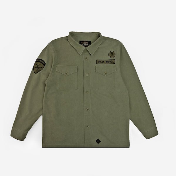 The photo shows a military style shirt jacket. The jacket is a thick canvas material and features 2 patches on the right chest and a patch on the left sleeve. The jacket has buttons as a closer and 2 chest pockets.