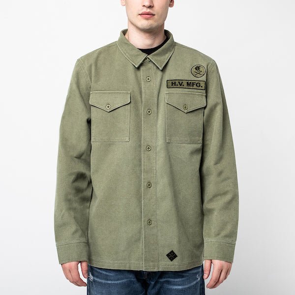 The photo shows a man in a military style shirt jacket. The jacket is a thick canvas material and features 2 patches on the right chest. The jacket has buttons as a closer and 2 chest pockets.