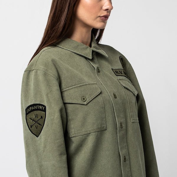 The photo shows a woman facing the right wearing a green military style shirt jacket. The photo is showing off the patch on the left sleeve.