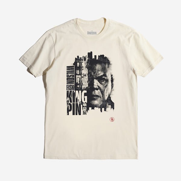 The photo is of an off-white colored tee. The tee features a gritty, high-contrast portrait of Wilson Fisk, also known as the Kingpin, with half of his face merging into a cityscape. His name, "Wilson Fisk," is stacked vertically, while "KINGPIN" and "OF CRIME" are displayed in bold, blocky typography. The design emphasizes his dominance over the criminal underworld, with the Daredevil "DD" logo in the lower corner.