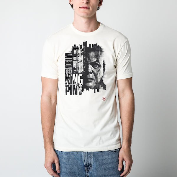 A Man standing in an off-white colored tee. The tee features a gritty, high-contrast portrait of Wilson Fisk, also known as the Kingpin, with half of his face merging into a cityscape. His name, "Wilson Fisk," is stacked vertically, while "KINGPIN" and "OF CRIME" are displayed in bold, blocky typography. The design emphasizes his dominance over the criminal underworld, with the Daredevil "DD" logo in the lower corner.