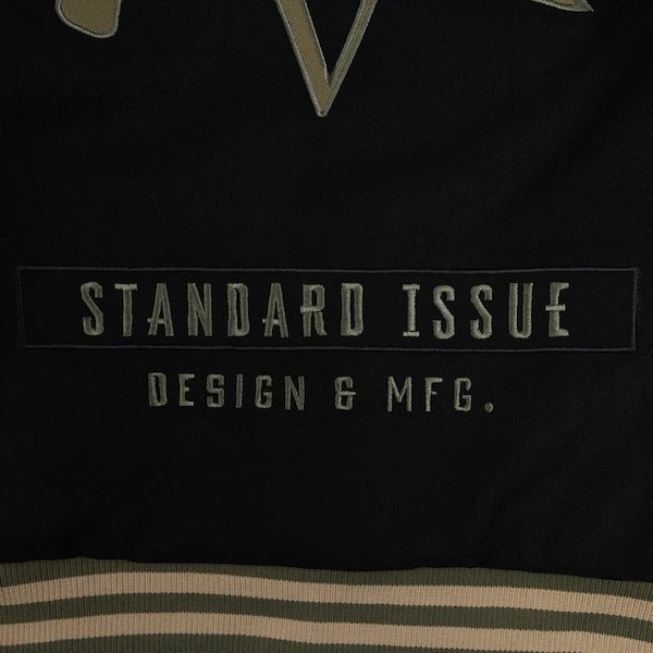 The photo shows a close up of embroidery on the lower back of a jacket. The embroidery text says "Standard Issue Design & MFG."