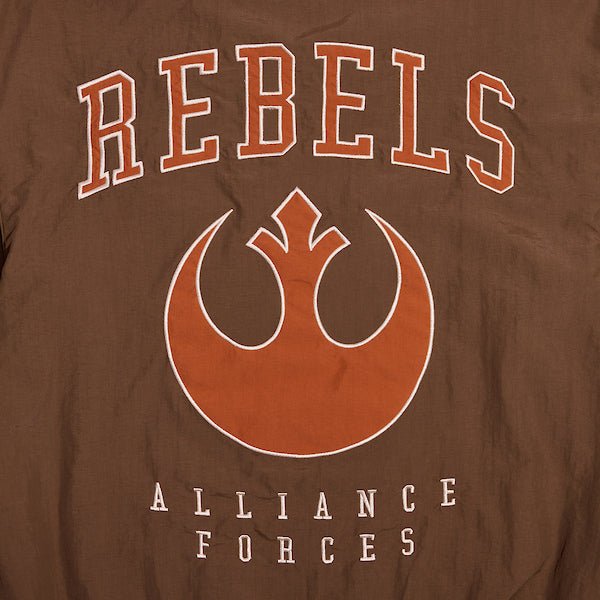 A close up of the back of a Star Wars-themed hooded windbreaker jacket, primarily brown with orange accents. The design features large, bold text reading 'REBELS' across the upper back, with the Rebel Alliance emblem in orange below it. Beneath the emblem, the words 'ALLIANCE FORCES' are printed in a smaller font. The jacket has an elastic waistband and cuffs, with a color-blocked pattern matching the front design.