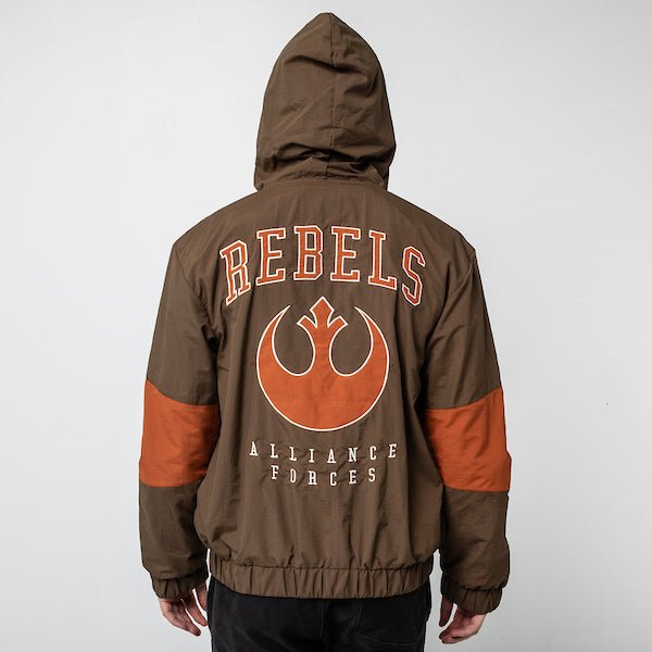 A person standing backwards to show the back of a Star Wars-themed hooded windbreaker jacket. The jacket is primarily brown with orange accents. The design features large, bold text reading 'REBELS' across the upper back, with the Rebel Alliance emblem in orange below it. Beneath the emblem, the words 'ALLIANCE FORCES' are printed in a smaller font. The jacket has an elastic waistband and cuffs, with a color-blocked pattern matching the front design.