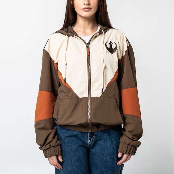 A Woman in a Star Wars-themed hooded windbreaker jacket featuring a Rebel Alliance emblem on the left chest. The jacket has a color-blocked design in brown, beige, and orange, with a front zipper, adjustable drawstrings on the hood, elastic cuffs, and two zippered pockets. The overall aesthetic is inspired by the Rebel pilot uniforms from the Star Wars universe