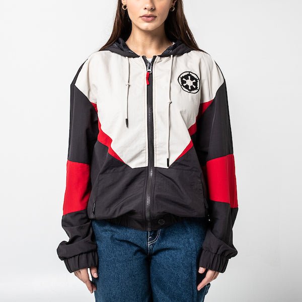 A woman in a Star Wars-themed hooded windbreaker jacket featuring a Imperial Army emblem on the left chest. The jacket has a color-blocked design in Black, White and Red, with a front zipper, adjustable drawstrings on the hood, elastic cuffs, and two zippered pockets.