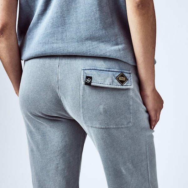 close-up of a person wearing blue sweatpants with a back pocket featuring two small patches—one with the Star Wars logo in a yellow diamond shape