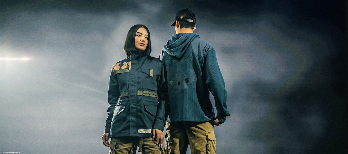 Two people in dark, Star Wars Rebel Pathfinders jackets standing against a stormy sky.