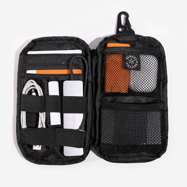 The same pouch is opened, revealing multiple compartments and elastic straps for organizing small items. Inside, there are mesh pockets and elastic loops holding various essentials, including charging cables, a power bank, pens, and a small orange case. A "Heroes & Villains" label is visible on the inner pocket.