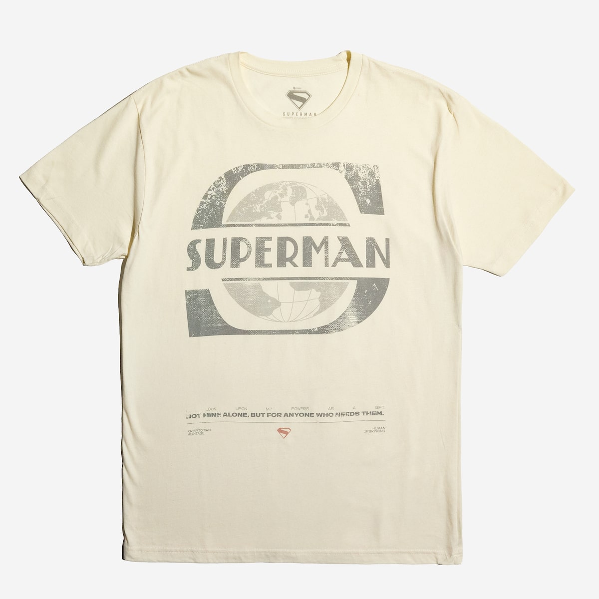 Cream-colored T-shirt featuring a distressed Superman logo and text, with additional small text and symbols printed near the bottom hem.