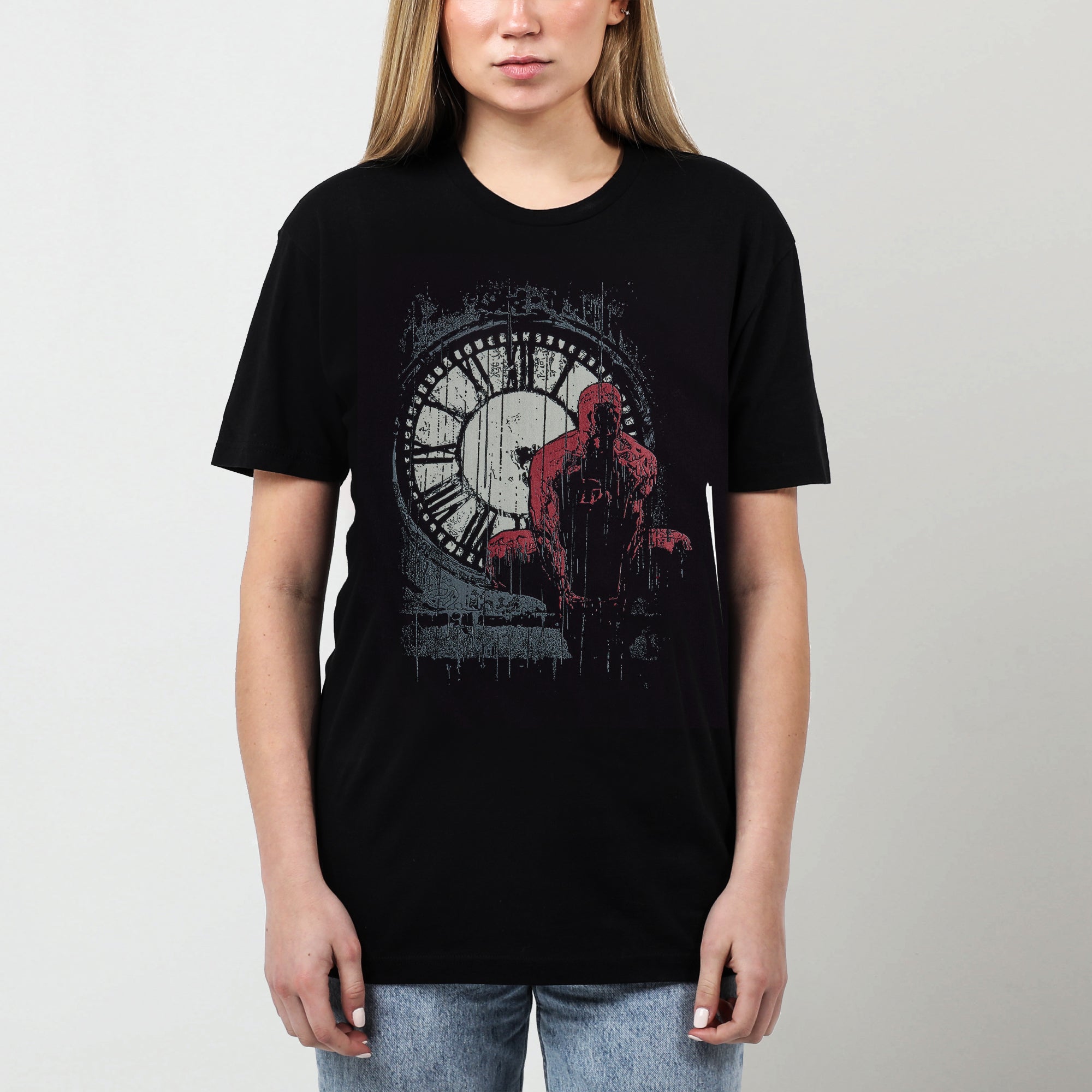 A female model featuring a moody graphic tee featuring Daredevil crouched in front of a weathered clock tower, drenched in rain. The distressed artwork and bold red highlights capture the grit and intensity of Hell’s Kitchen’s vigilante.
