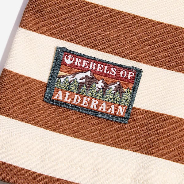 Photo shows a close up of a t-shirt with white and orange horizontal stripes. The close up shows a rectangular patch with the words "Rebels of" at the top and "Alderaan" at the bottom. Between the words is a small picture of a forest and mountains.