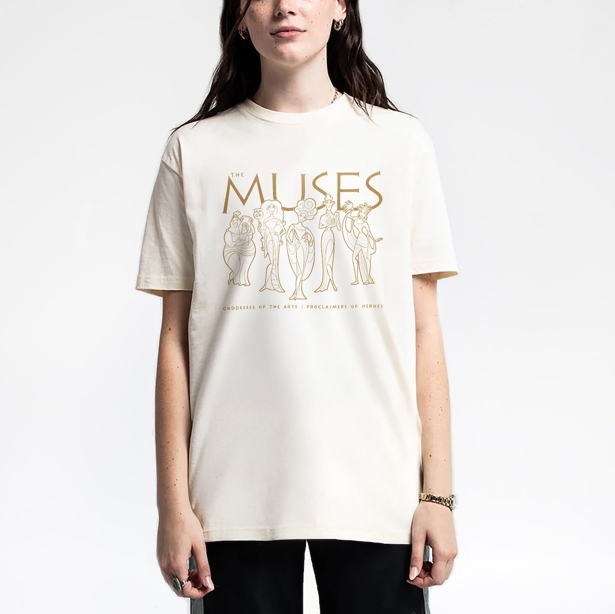 Woman in a cream T-shirt with graphic drawings of five characters and text reading "THE MUSES."