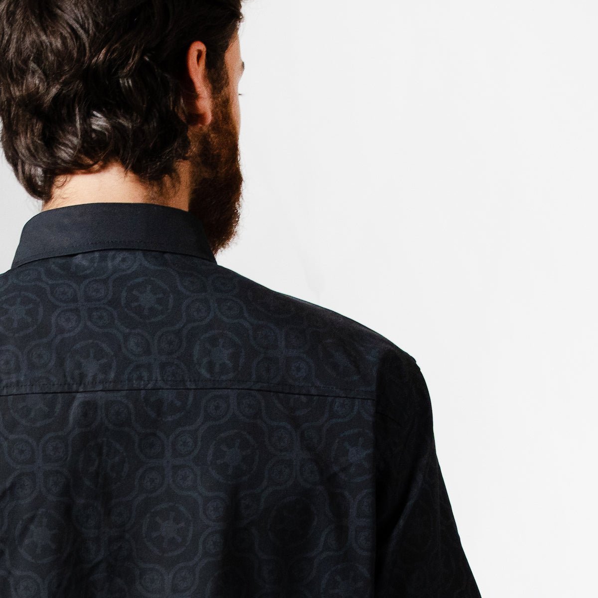 A close up of a man in a button up black shirt with red details in a star wars imperial geometric pattern