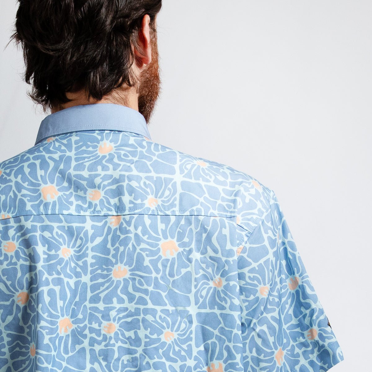 A close up of a man standing backwards in a blue button down star wars rebel shirt with 60s inspired patterns