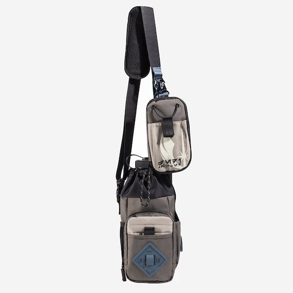 The photo shows a crossbody bag designed for carrying a water bottle. The bag features a drawstring closure at the top, a front zippered pocket, and a blue rubber patch with a geometric design meant for attaching a clip. The adjustable black strap has a padded section for comfort and a blue cord with holes to attach clips and a tech organizer bag. The bag is in a subtle brown with pops of blue and black.
