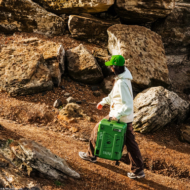 Person walking with a green star wars grogu themed suitcase in a rocky outdoor setting