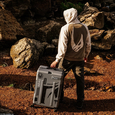 Person in a hoodie with Mudhorn Logo carrying a matching Star Wars Mandalorian suitcase in a rocky outdoor setting