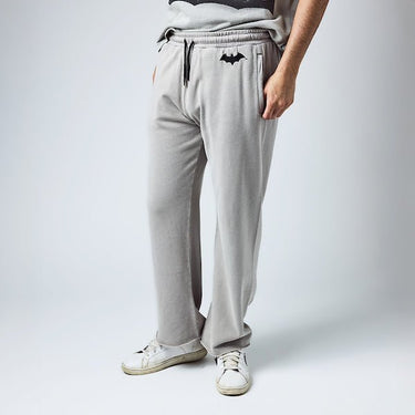 Man in light gray sweatpants with an elastic waistband and black drawstring, featuring a small black Batman logo near the left pocket and a vertical "Gotham City" graphic printed in distressed black text along the lower left leg.