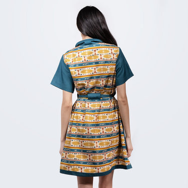 A woman standing backwards in a button up yellow and teal dress thats star wars jedi inspired with a striped tapestry pattern 