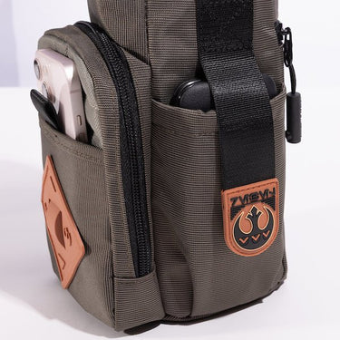 The photo shows a close up of a pocket on the bag. The pouch has a black strap with orange rubber on the end. The Orange Rubber has raised black art to showcase the Rebel logo. 