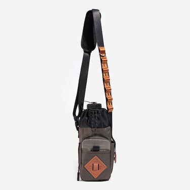 The photo shows a crossbody bag designed for carrying a water bottle. The bag features a drawstring closure at the top, a front zippered pocket, and an orange rubber patch with a geometric design meant for attaching a clip. The adjustable black strap has a padded section for comfort and a blue cord with holes to attach clips and a tech organizer bag (Not pictured). The bag is in a subtle brown with pops of orange and black.