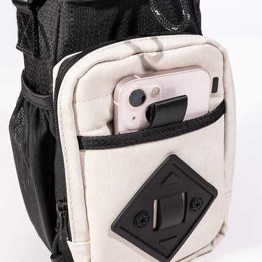 The photo shows a close up of the bags  white main outer zipper pouch. The pouch has a black diamond shaped rubber patch on the front. There is a pocket on this pouch showing an iphone being held. 