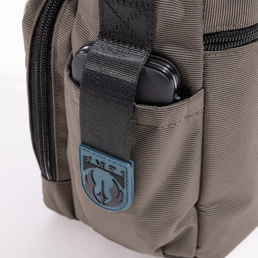 The photo shows a close up of a pocket on the bag. The pouch has a black strap with blue rubber on the end. The Blue Rubber has raised black art to showcase the jedi logo. 