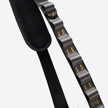 The photo shows a close up detailing of the shoulder strap. Featured is the grey and gold decorative detailing. The detailing has loops for attaching clips and a tech case. The top loop has a "D"-Ring attached.