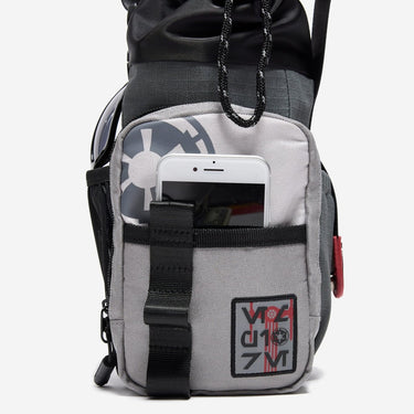 The photo shows a close up of the bags main outer zipper pouch. The pouch has an star wars imperial patch on the bottom right and an imperial cog logo printed on the top left. There is a pocket on this pouch showing an iphone being held. 