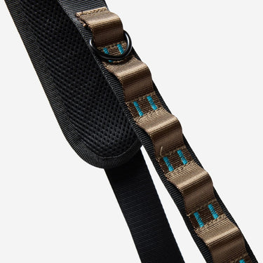 The photo shows a close up detailing of the shoulder strap. Featured is the brown and blue decorative detailing. The detailing has loops for attaching clips and a tech case. The top loop has a "D"-Ring attached.