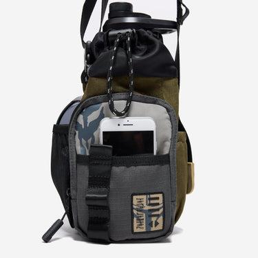 The photo shows a close up of the bags main outer zipper pouch. The pouch has an star wars mandalorian patch on the bottom right and an mythosaur logo printed on the top left. There is a pocket on this pouch showing an iphone being held. 