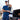 Man in blue athletic fantastic four shirt and cap with a backpack, standing next to an open truck bed.