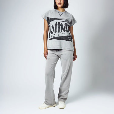 A woman dressed in a grey sleeveless crew neck and grey wide leg sweatpants, featuring a Batman themed lounge set