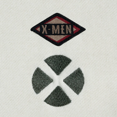 A dip-dyed hoodie in cream and green featuring X-Men's Rogue and Gambit. The front displays a small X-Men logo, while the back showcases a black-and-white comic-style illustration of Rogue and Gambit embracing, with the word "Sugah" below.