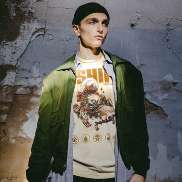 A male model styled as alt/ grunge wearing A natural-colored Magic: The Gathering t-shirt featuring Redshift, the Rocketeer Chief, in a chaotic, steampunk-inspired vehicle with a massive rocket strapped to the back. The goblin-like character has wild white hair, glowing eyes, and a mischievous grin as he speeds forward. The distressed artwork includes grunge-style textures, the bold text 'Red Shift' at the top, and Magic: The Gathering mana symbols along the bottom."