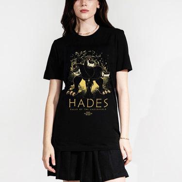 Woman in a black tee with an Illustration of a three-headed dog with a shadowy figure, hades, in front of it, set against an abstract background.