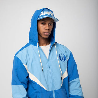 A man in a Star Wars-themed hooded windbreaker jacket with a matching hat. The windbreaker features a Jedi Knights emblem on the left chest. The jacket has a color-blocked design in Blue, Light Blue and White, with a front zipper, adjustable drawstrings on the hood, elastic cuffs, and two zippered pockets. 