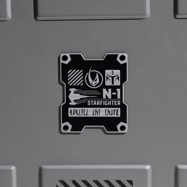 Close up of Metallic badge on the back of a Mandalorian themed suitcase with 'N-1 Starfighter' text on a gray background