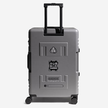 Gray suitcase with black wheels and a handle on a white background in the center of the suitcase is a metal badge with star wars Mandalorian themed details
