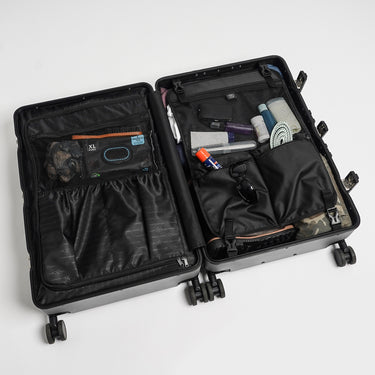 Open Mandalorian Suitcase with travel items in some of the various compartments on a white background